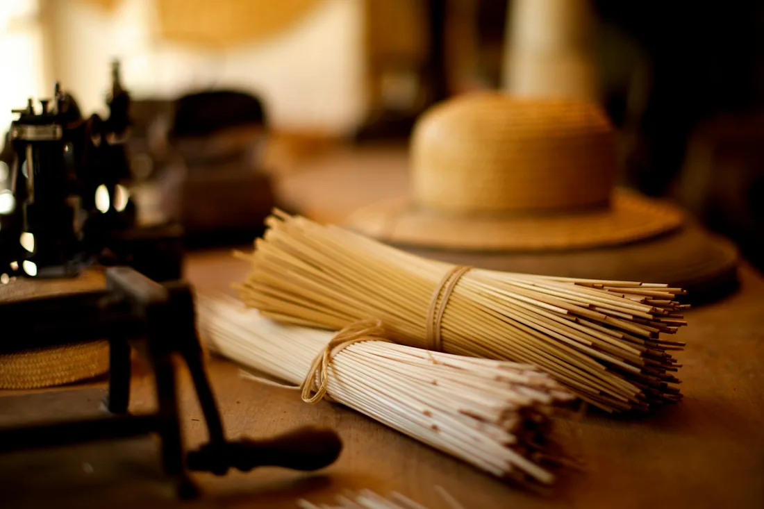 Haces de paja atados y un sombrero de paja sobre la mesa de madera de un taller de sombrerería